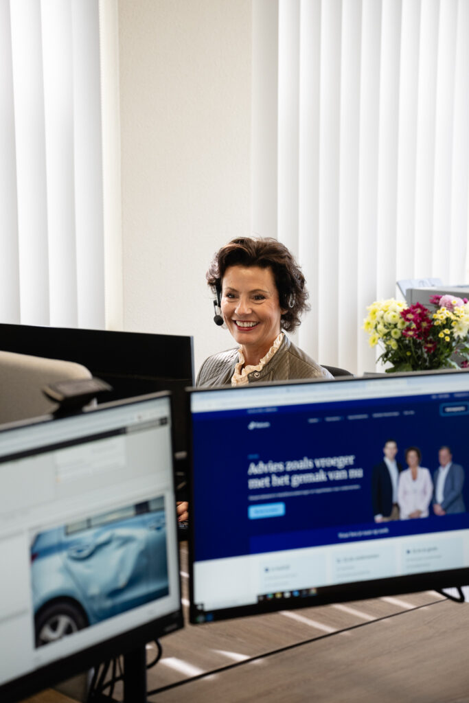 Vrouw met headset achter computerschermen op kantoor.